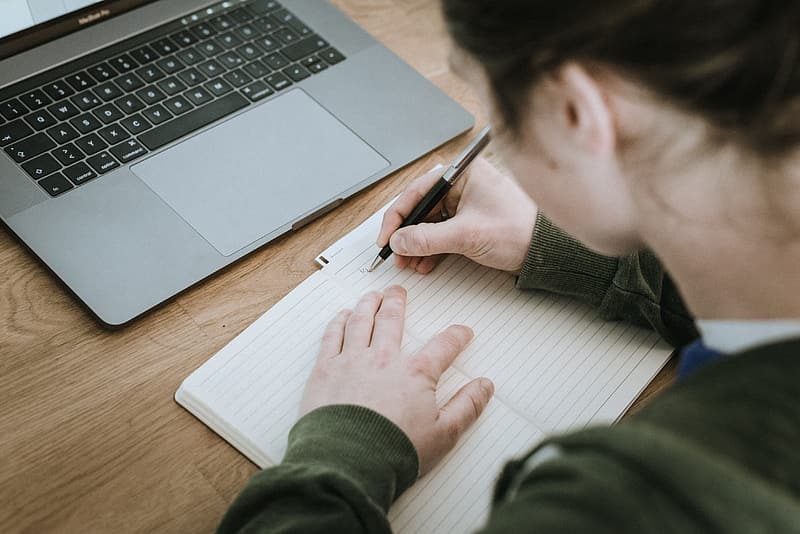 Woman_writing_on_lined_paper_near_macbook_pro